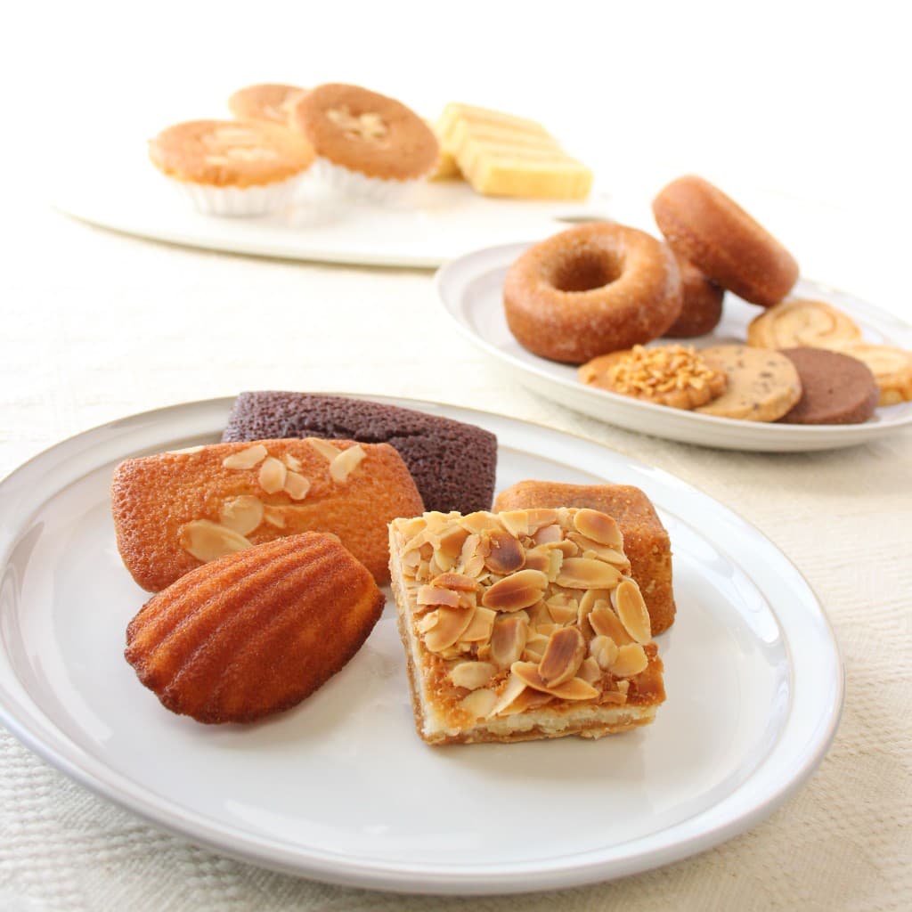 白い皿に並べたマドレーヌ、フィナンシェ、クッキーなど焼き菓子の詰め合わせ